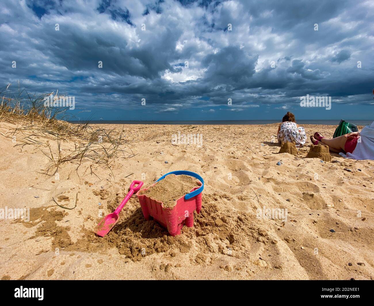 Pink Basket und Spaten auf Great Yarmouth Strand in einem kalten Sommertag, traditionelle englische Küste, Himmel mit Wolken keine Menschen, große Strecke des Sandes, Großbritannien sein Stockfoto