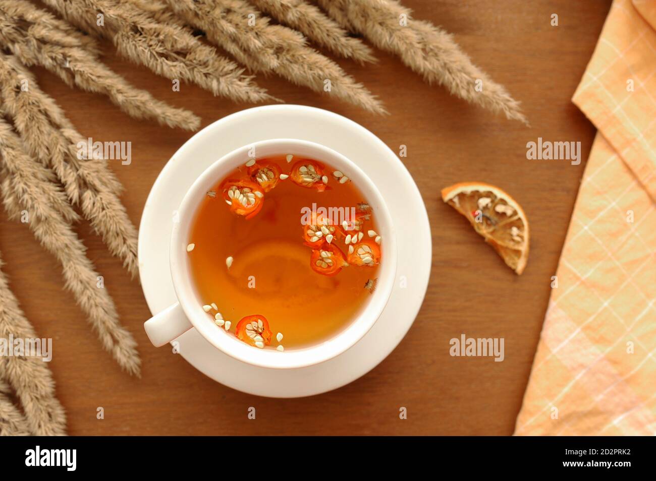 Gemütliches Herbstfrühstück mit nützlichem Tee, Honig, Zimt-Sticks, Zitrone, Dogrosenbeeren und Bouquet von getrockneten Blumen und Baumwolle orange Serviette für servin Stockfoto