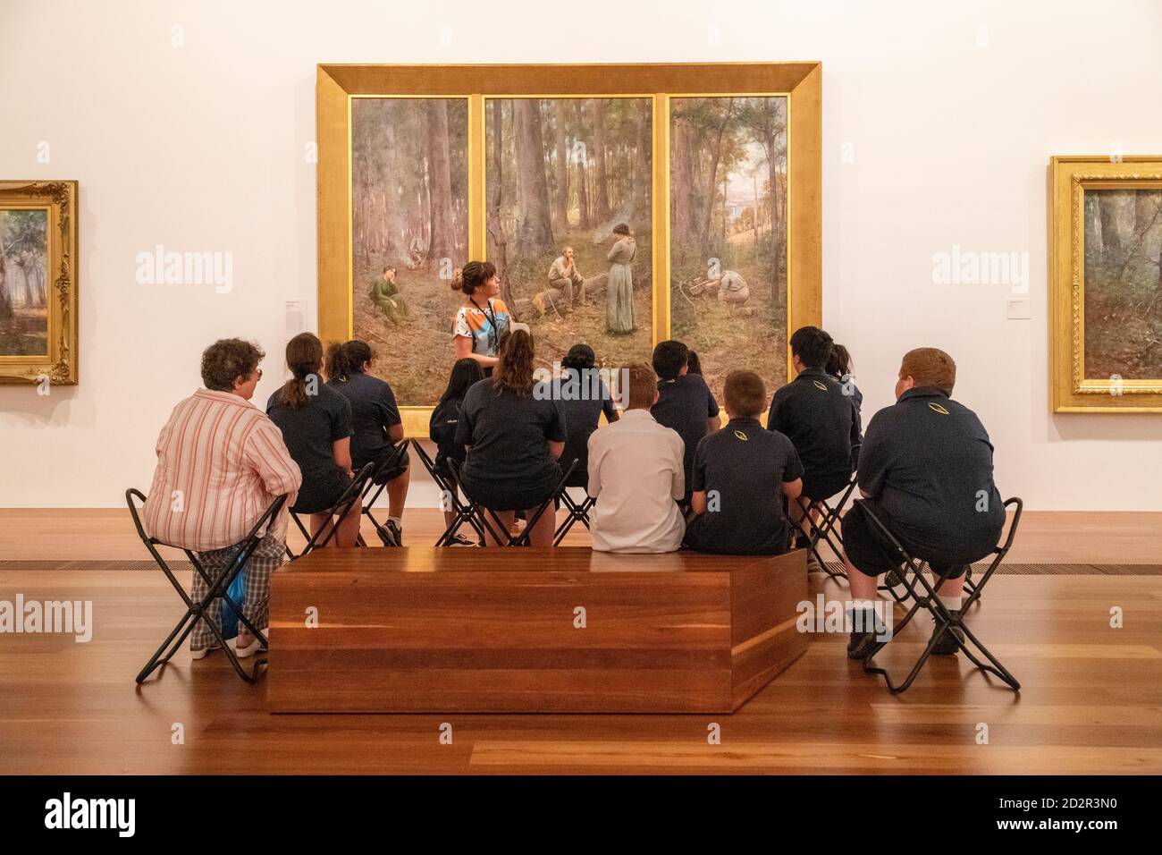 Die Schüler hören einem Führer zu, der in der National Gallery of Victoria über ein Gemälde spricht. Stockfoto