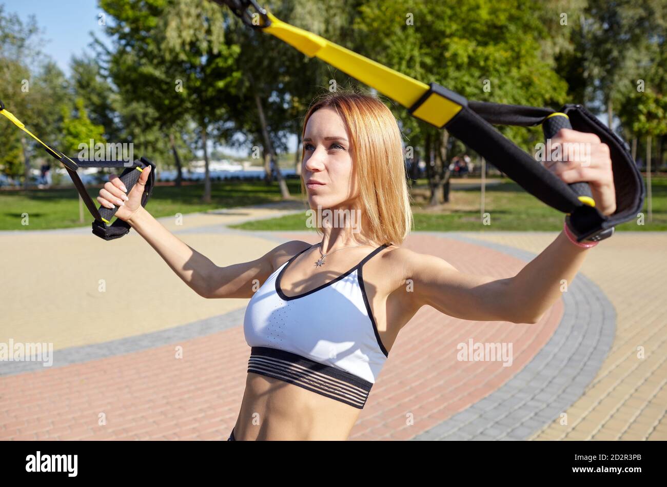 Durchführen von TRX-Übungen. Junge athletische Frau mit perfektem Körper in Sportbekleidung trainiert ihre Arme mit trx Fitnessbändern im Stadtpark Stockfoto