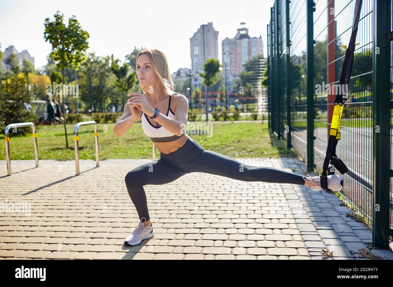 Durchführen von TRX-Übungen. Junge athletische Frau in Sportbekleidung Trainingsbeine mit trx Fitnessriemen im Stadtpark Stockfoto
