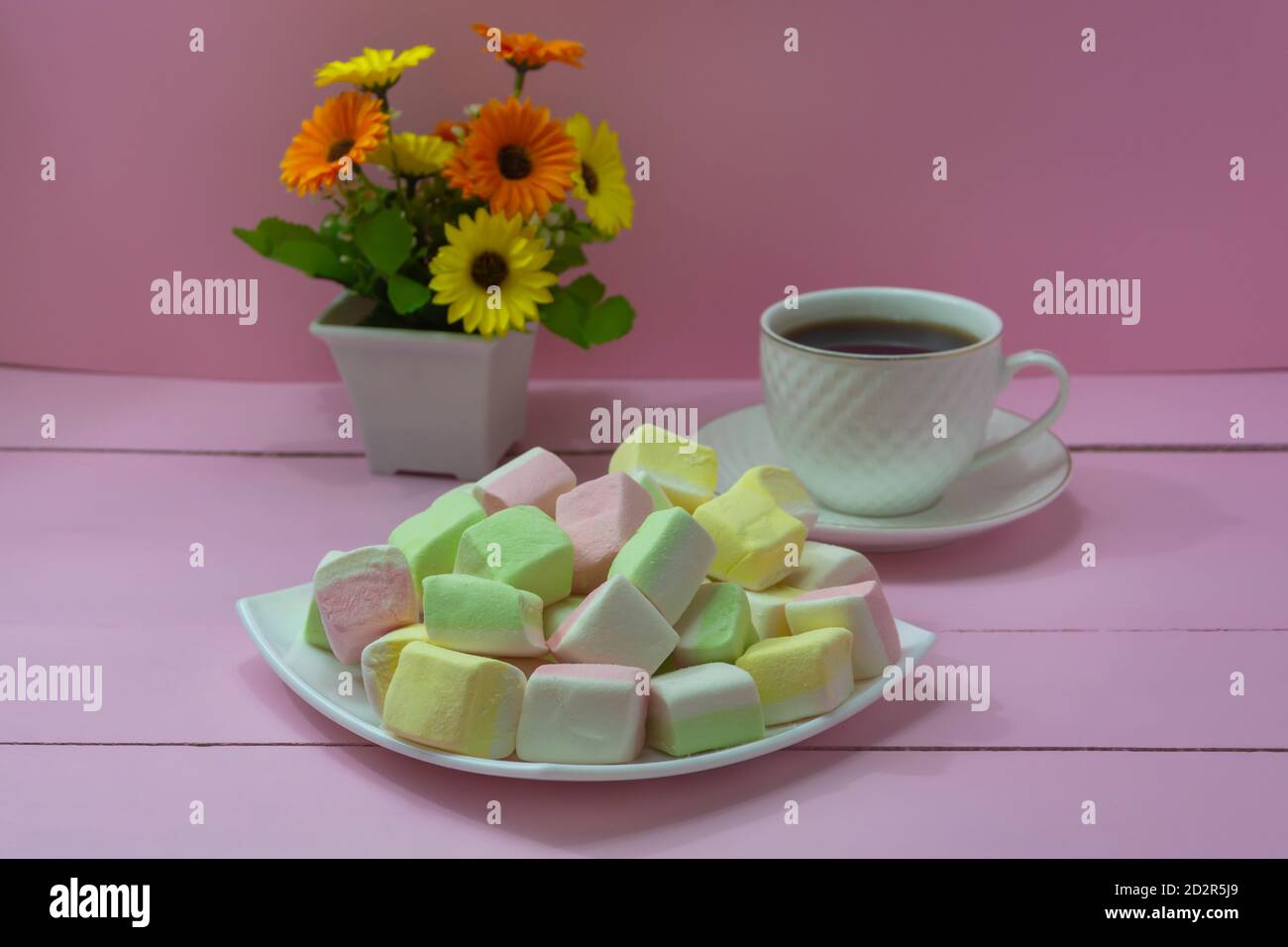 Marshmallows aus verschiedenen Früchten auf weißen Schale Nahaufnahme. Eine Tasse starken Kaffee auf einem rosafarbenen Holztisch. Kaffeepause, romantische Stimmung. Stockfoto