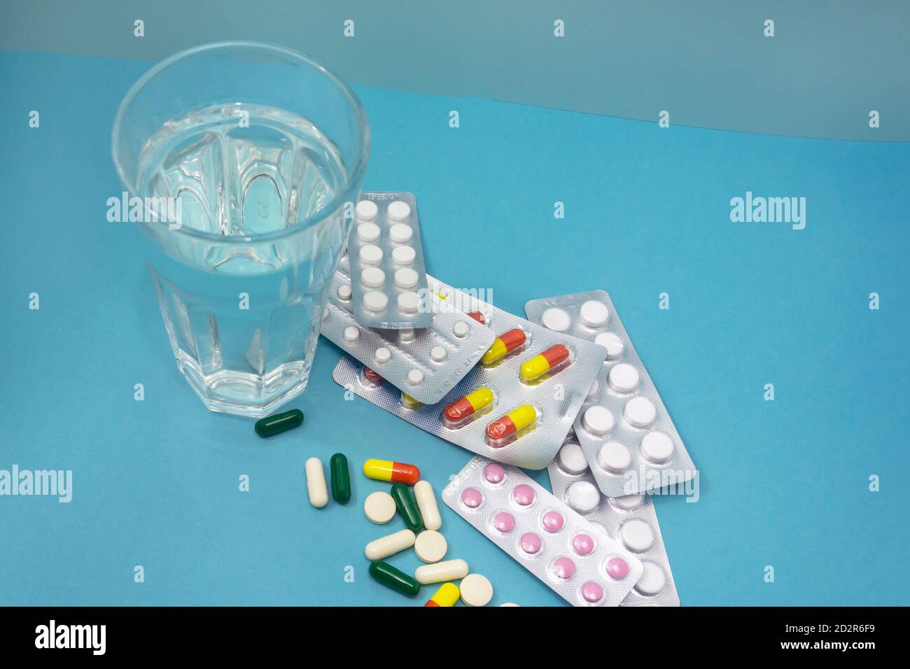 Medikamente in Tabletten und Kapseln auf blauem Hintergrund. Ein Glas sauberes Wasser. Zeit, Ihre Medizin zu nehmen. Apotheke, Krankenhaus, Medizin Konzept. Stockfoto