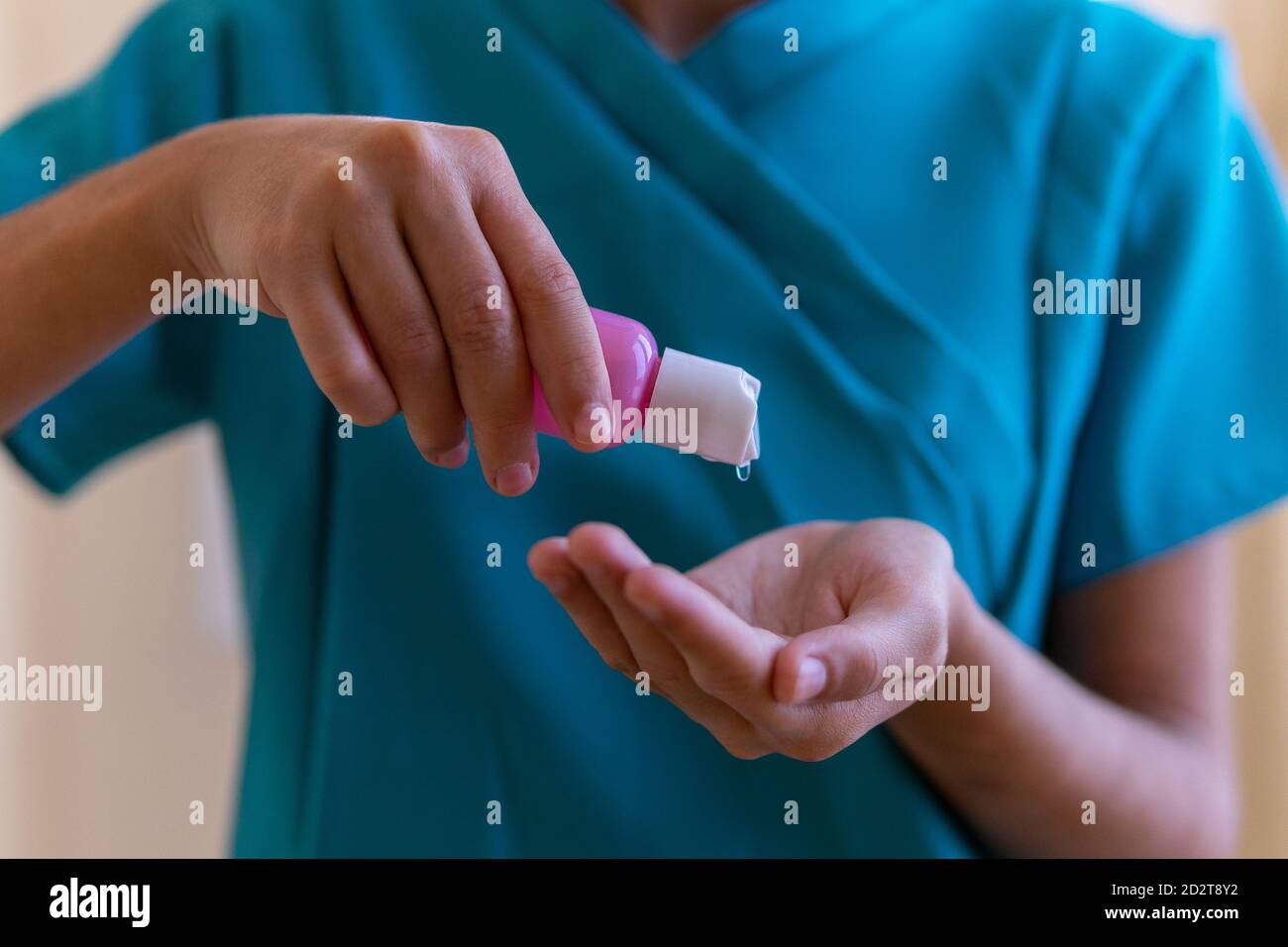 Crop von jungen Krankenschwester in blauen Peelings und medizinische Maske Anwendung von Desinfektionsmittel auf die Hände während der Vorbereitung auf den Eingriff in der Klinik Stockfoto