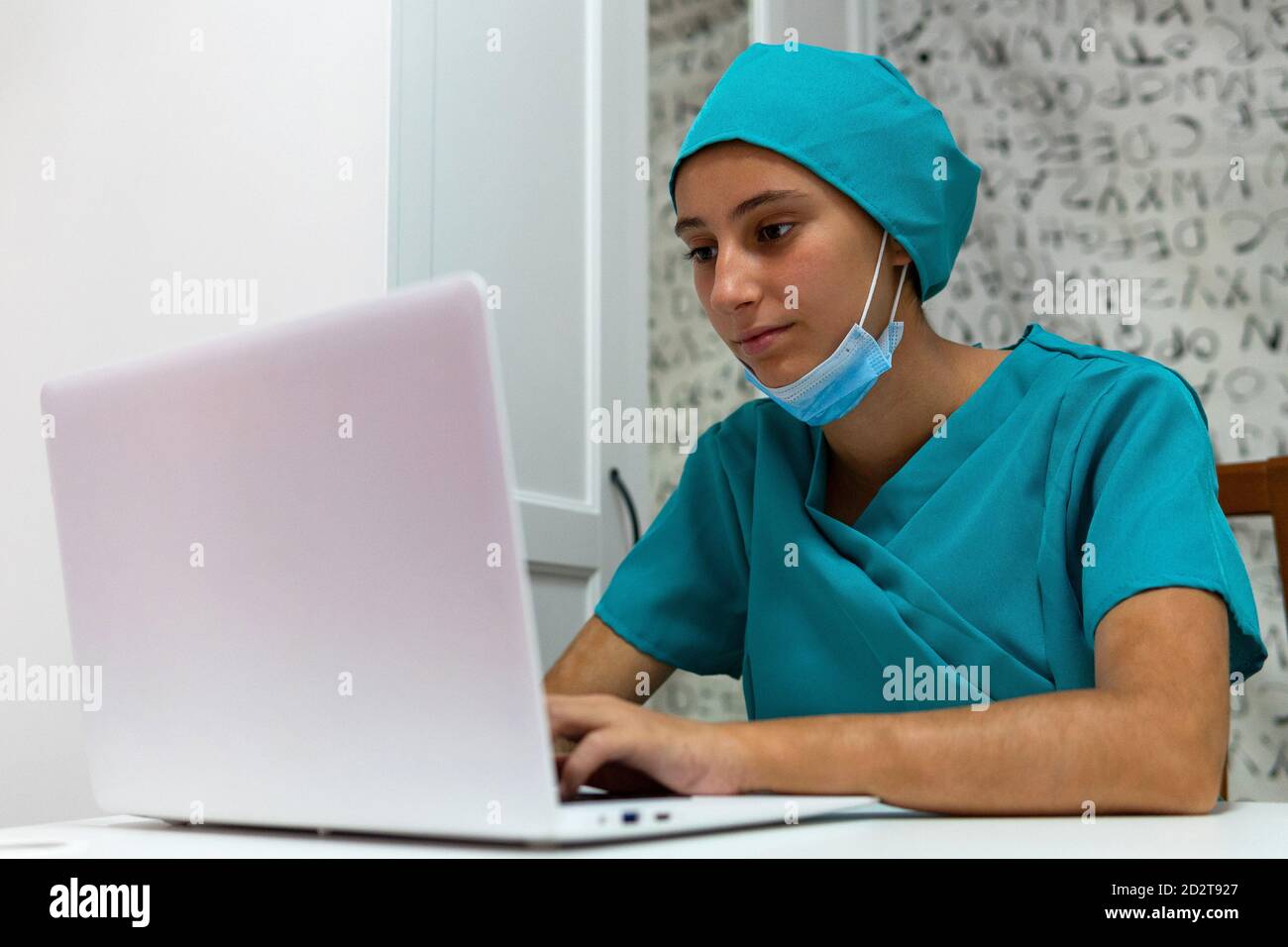 Junge Krankenschwester in blauer Uniform sitzt am Tisch und mit Laptop während der Arbeit im Krankenhaus Stockfoto