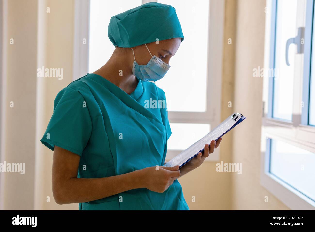 Konzentrierte junge Krankenschwester in blauer Uniform und Maske macht medizinische Hinweise zur Zwischenablage während der Arbeit im Krankenhaus Stockfoto
