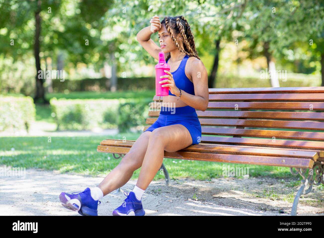 Seitenansicht der hispanischen Athletin auf der Bank sitzend mit Eine Flasche Wasser nach dem Training im Park Stockfoto