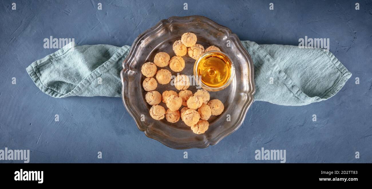 Ansicht von oben auf Amaretti, traditionelle italienische Mandelkekse, mit Amaretto Likör, Panorama über dem Kopf mit Kopierraum, auf dunkelblauem Hintergrund Stockfoto