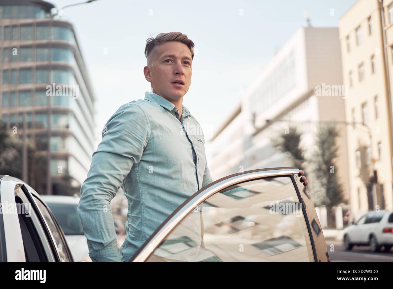 Schöner männlicher Fahrer schaut weg immer aus modernen Automobil, während Stehen auf dem Parkplatz in der Stadt Stockfoto