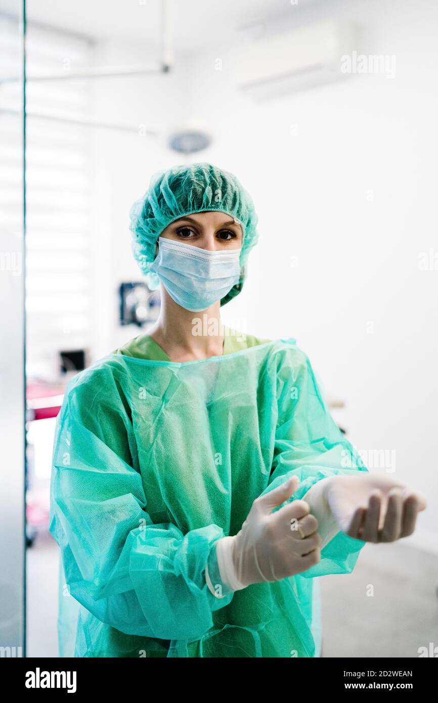 Ernsthafte weibliche Tierarzt Chirurg in Maske und Uniform setzen auf Schutzhandschuhe und Vorbereitung auf den Betrieb während des Stehens in Betrieb Theater der Tierklinik und Blick auf die Kamera Stockfoto