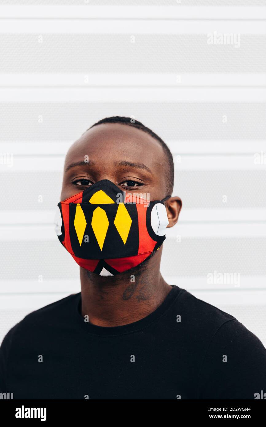 Nahaufnahme Porträt eines afroamerikanischen Mannes mit einer bunten Maske. Er blickt mit ernsthafteren Worten auf die Kamera Stockfoto