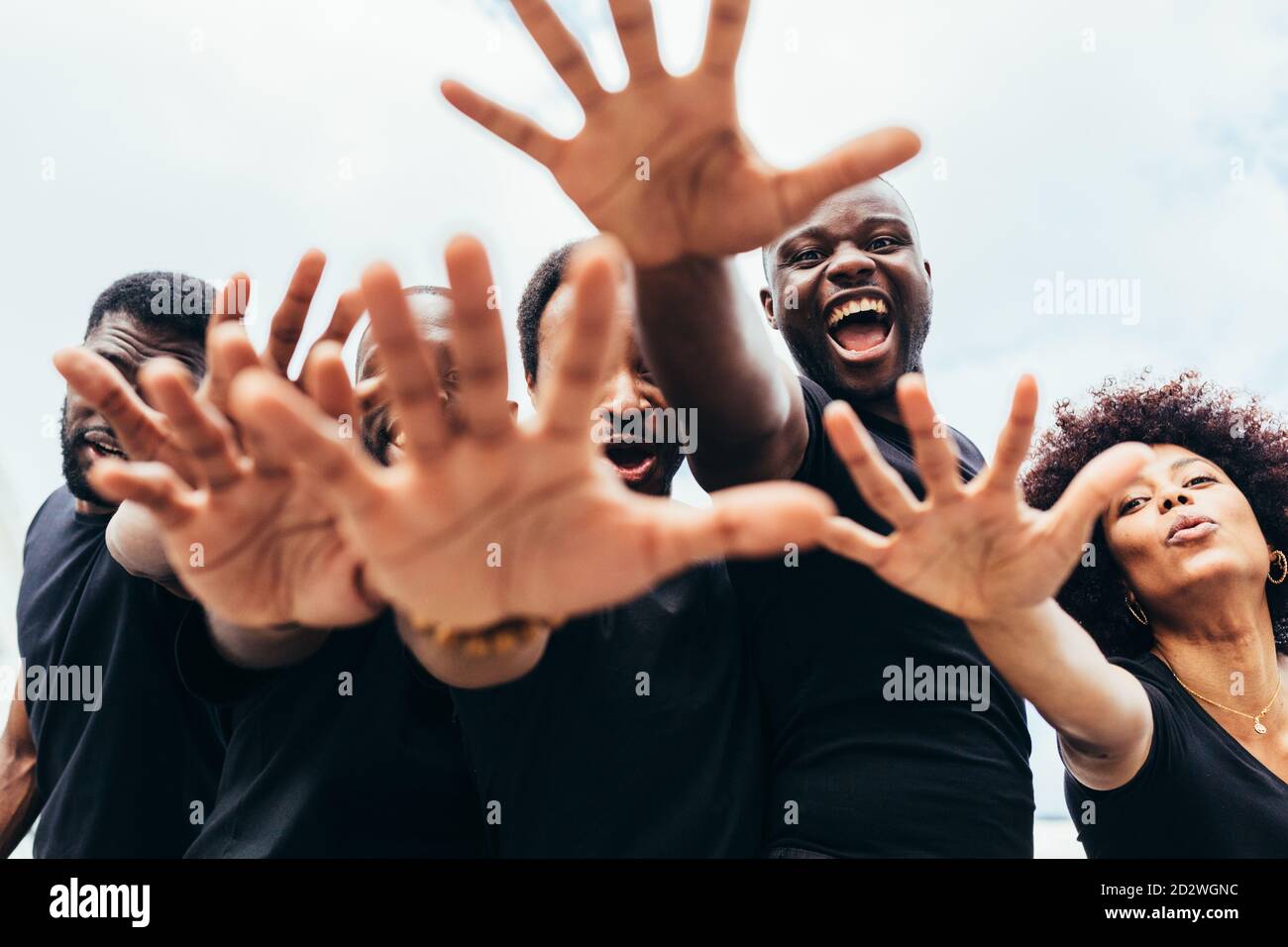 Fröhliche schwarze Männer und Frauen, die die Hände gegen einen blauen Himmel heben Stockfoto