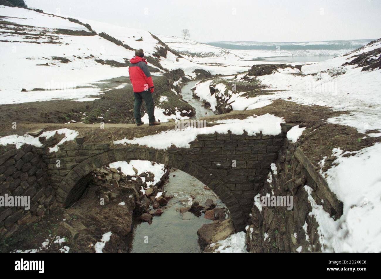 Trotz Temperaturen unter Null und starkem Schneefall, der Grad des Thruscross Reservoir in North Yorkshire, die Notarität gewann während der Sommertrockenheit ermöglicht die lange seit überschwemmten Dorf West End zu sehen. Das Niveau ist niedriger als je zuvor als einjähriger Wanderer auf der alten Reitpferdebrücke, die heute gefunden wurde. Foto von Paul Barker/PA Stockfoto