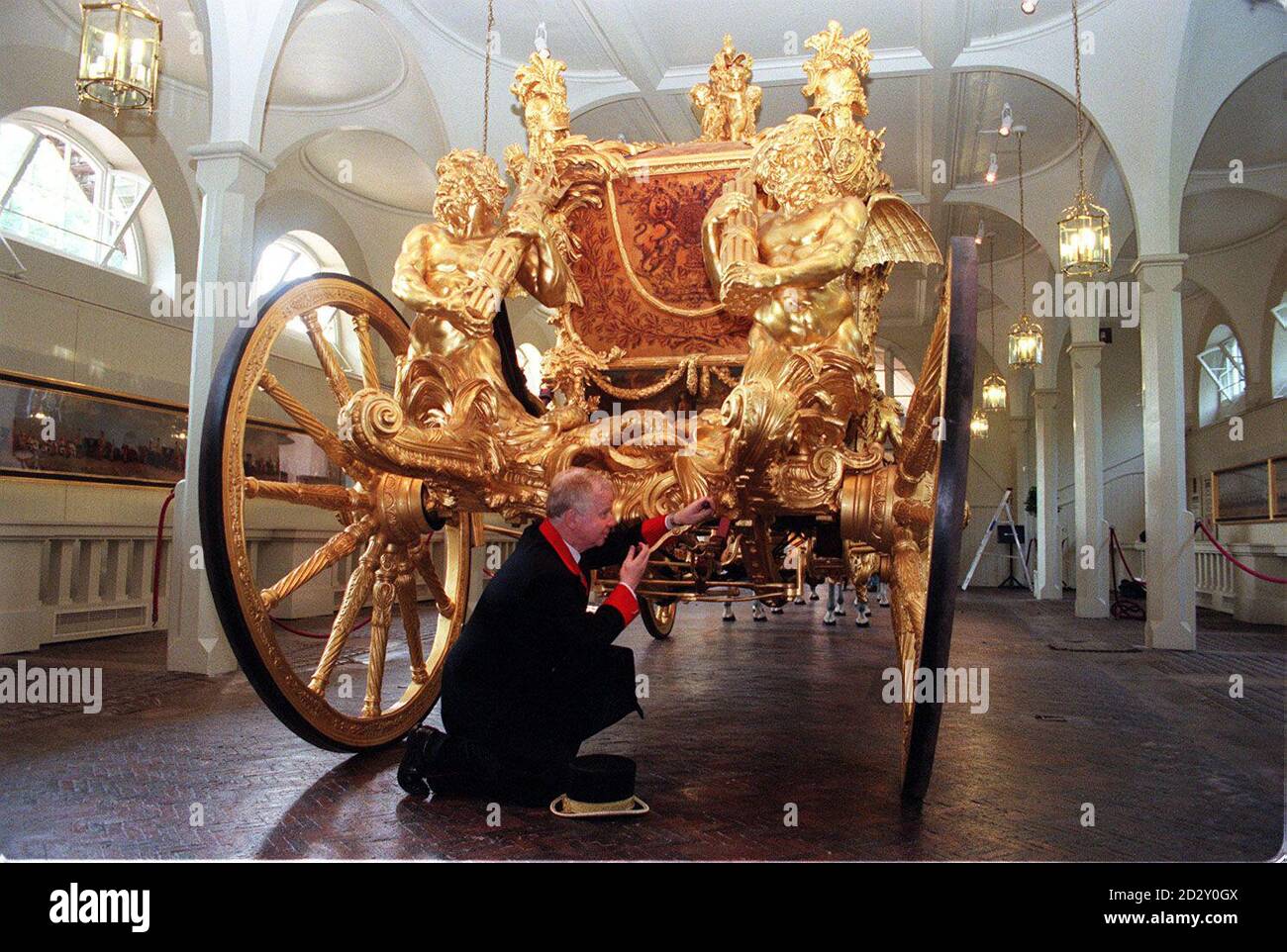 Der Gold State Coach, der seit Wilhelm IV. 1831 bei jeder Krönung verwendet wird, steht im Kutschenhaus der Königlichen Mews, wo er umgezogen wurde, um ihn vor den Elementen zu schützen. Der Leiter der Royal Collection, George Martin, wird im Royal Mews am Buckingham Palace als Hüter des königlichen Busses dargestellt. Stockfoto