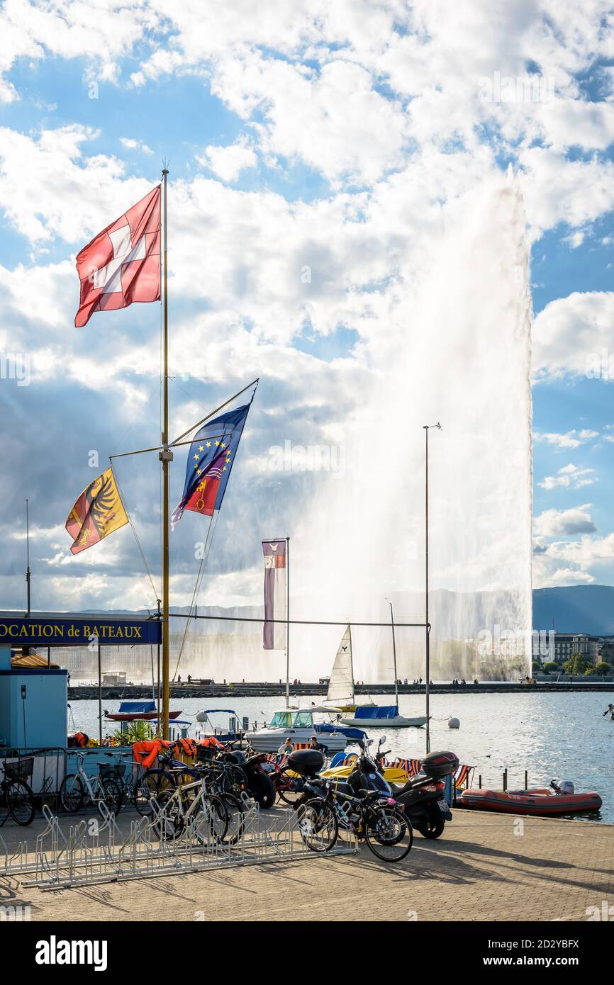Die Schweizer Flagge fliegt an einem stürmischen Tag am Ufer des Genfersees in Genf, Schweiz, mit dem Jet d'Eau Wasserstrahlbrunnen in der Ferne Stockfoto