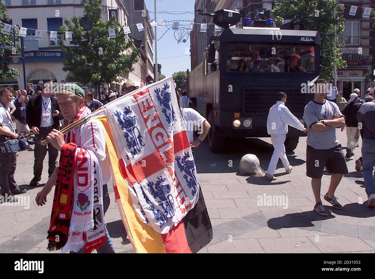 Auf dem Hauptplatz von Charleroi sitzt unter englischen und deutschen Fußballfans eine Polizeiwasserkanone. Vor dem Spiel kam es zu frischer Gewalt mit Engländern. Die belgische Polizei setzte eine Wasserkanone ein, nachdem englische und deutsche Fans auf dem Hauptplatz zu kämpfen begannen. Stockfoto