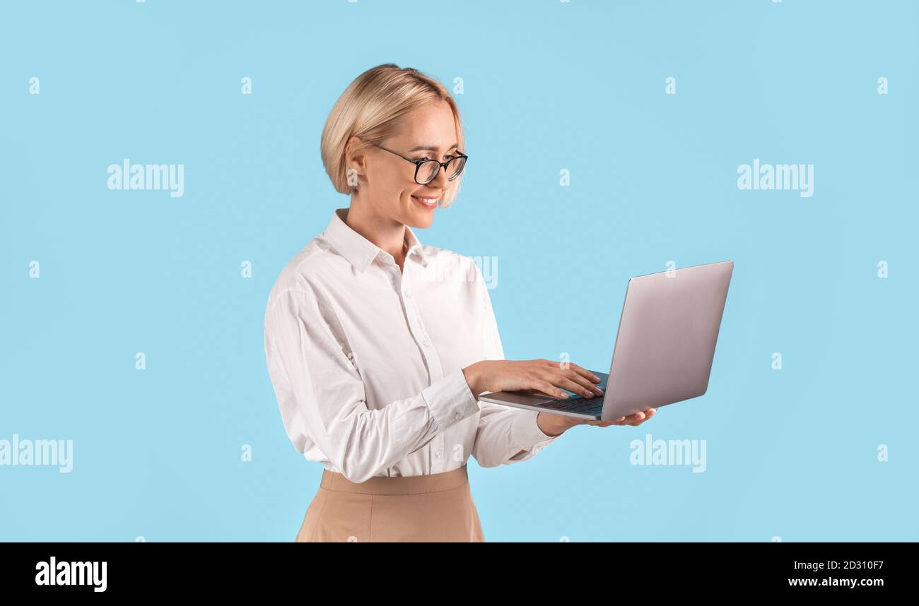 Glückliche Geschäftsfrau mit Laptop-Computer für Online-Arbeit oder Studien über blauen Studio-Hintergrund, Panorama Stockfoto
