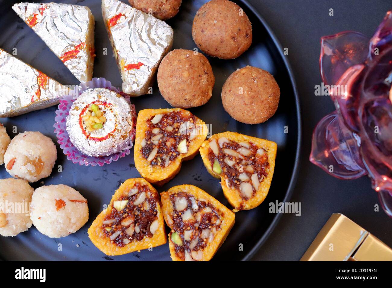 Verschiedene indische Süßigkeiten oder Mithai, Rava laddoo, Besan laddu, Trockenfrüchte Süßigkeiten in einem schwarzen Teller zusammen mit Happy Diwali Schokolade für Diwali Festival. Stockfoto