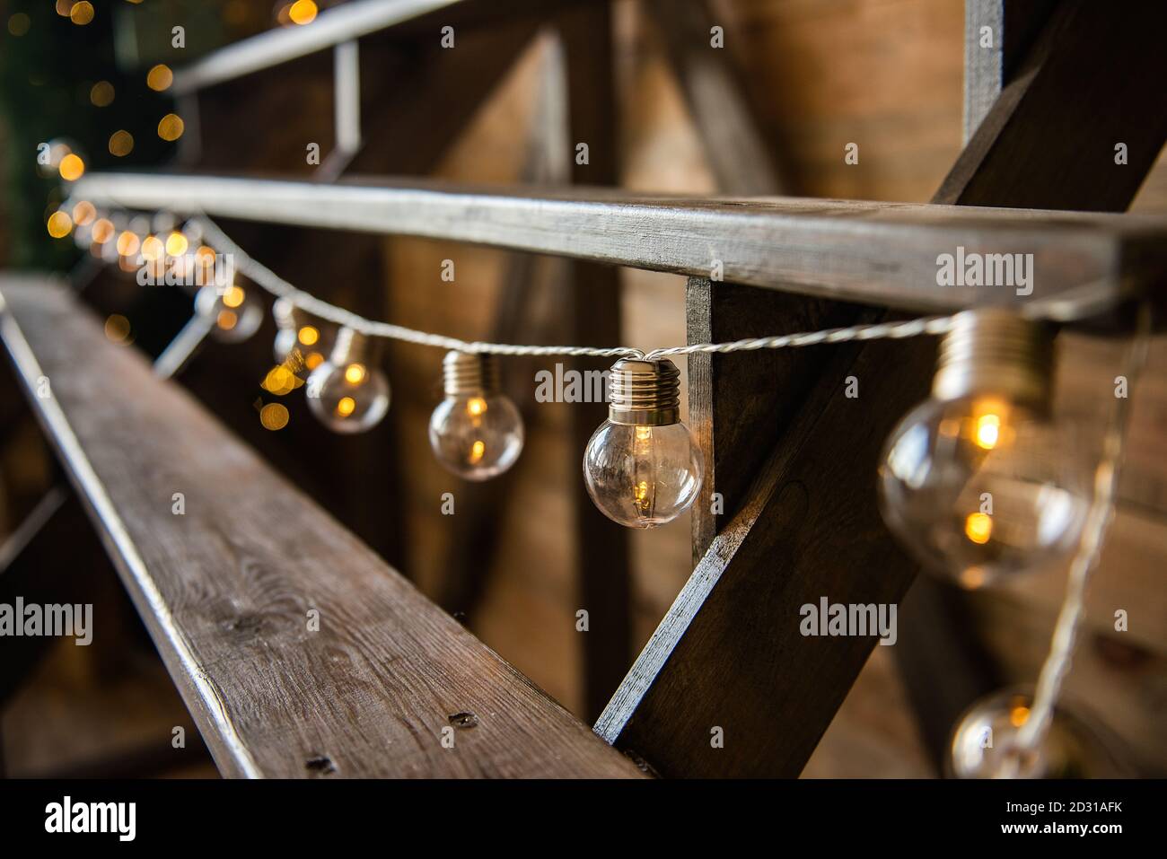 Weihnachtsgirlande von Glühbirnen, die von einer Holztreppe hängen. Festliche Heimtextilien. Skandinavischer Loft-Stil.Textur Hintergrund, Kopierraum Stockfoto