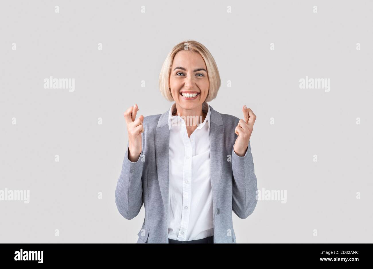Schöne kaukasische Geschäftsfrau in eleganten Anzug Überkreuzung Finger für Viel Glück über hellgrauen Studio Hintergrund Stockfoto