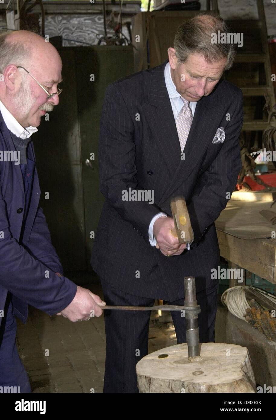 Der Prinz von Wales hilft, eine Münze zu schlagen, die an seinen Besuch erinnert, mit dem Schmied Rod Ledsham in der Schmiede während einer Tour durch Surrey Docks City Farm, South East London. Stockfoto