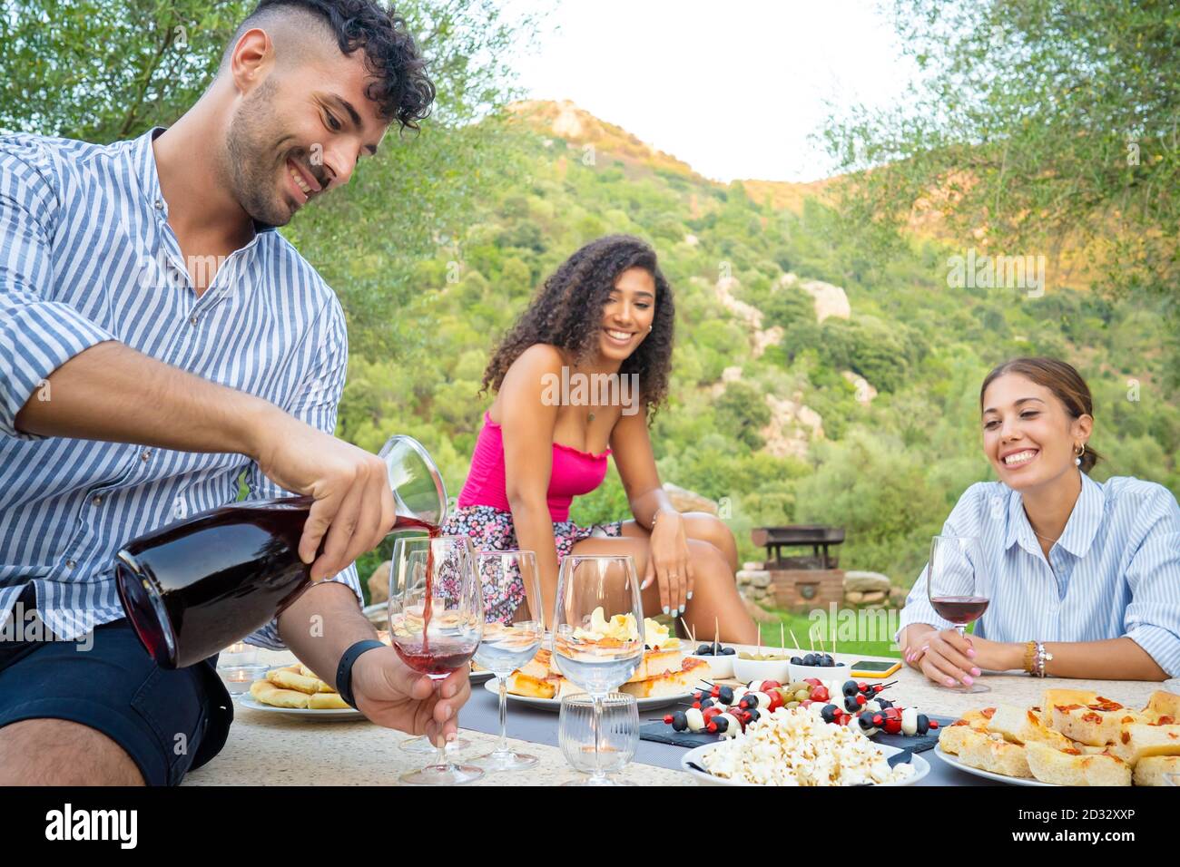 Gruppe von drei multiethnischen Freunden feiern im Freien - selektive Fokus Auf den jungen Mann mit einem gestreiften Hemd in rot Wein in das Glas zu seinem Stockfoto