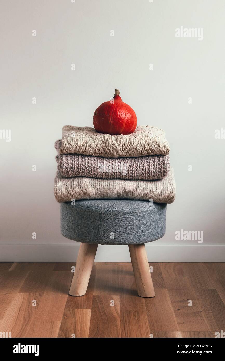 Ein Stapel gefalteter Pullover auf einem Hocker und orangefarbener Kürbis auf dem Hocker. Herbststimmung Konzept. Stockfoto