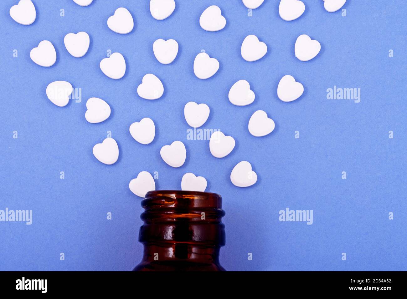 Herzförmige Pillen aus Flaschenglas auf blauem Hintergrund. Medikamente, die Menschen helfen. Stockfoto