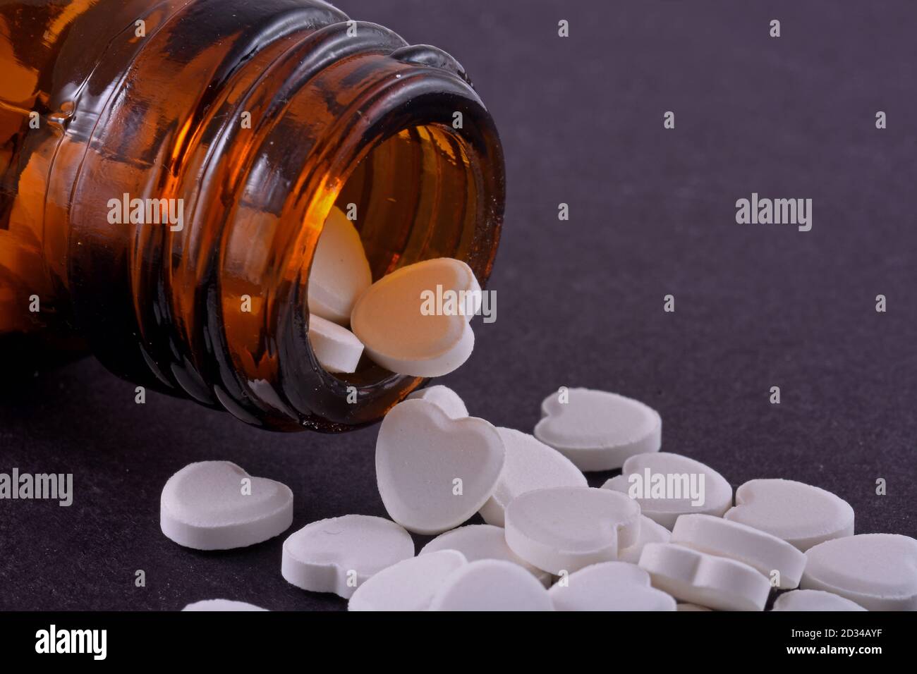 Herzförmige Pillen aus Flaschenglas auf schwarzem Hintergrund. Medikamente, die Menschen helfen. Stockfoto