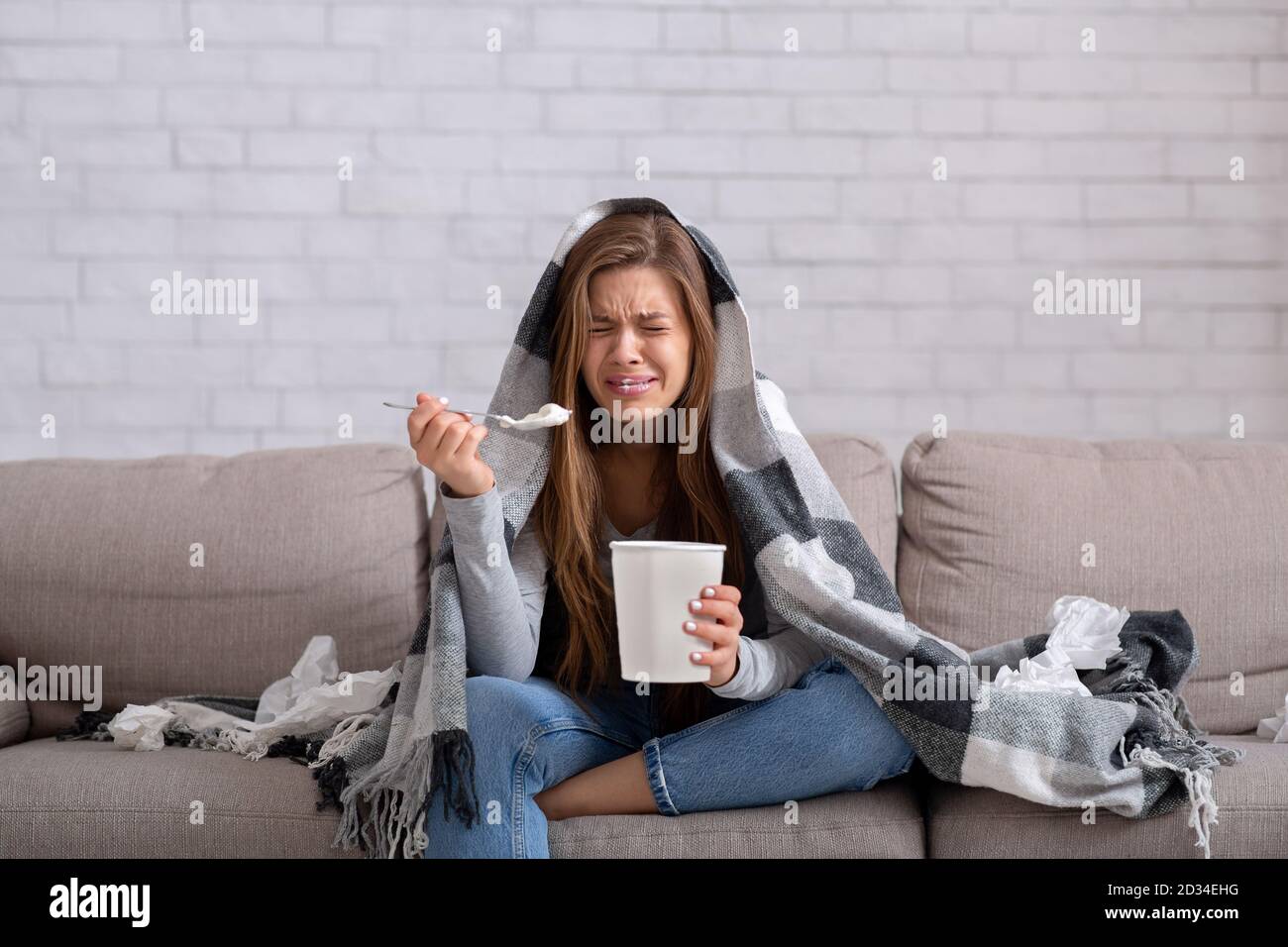 Herzgebrochene junge Frau, die Eis aus dem Eimer isst, während sie einen romantischen Film im Fernsehen sieht, sich deprimiert und einsam fühlt Stockfoto
