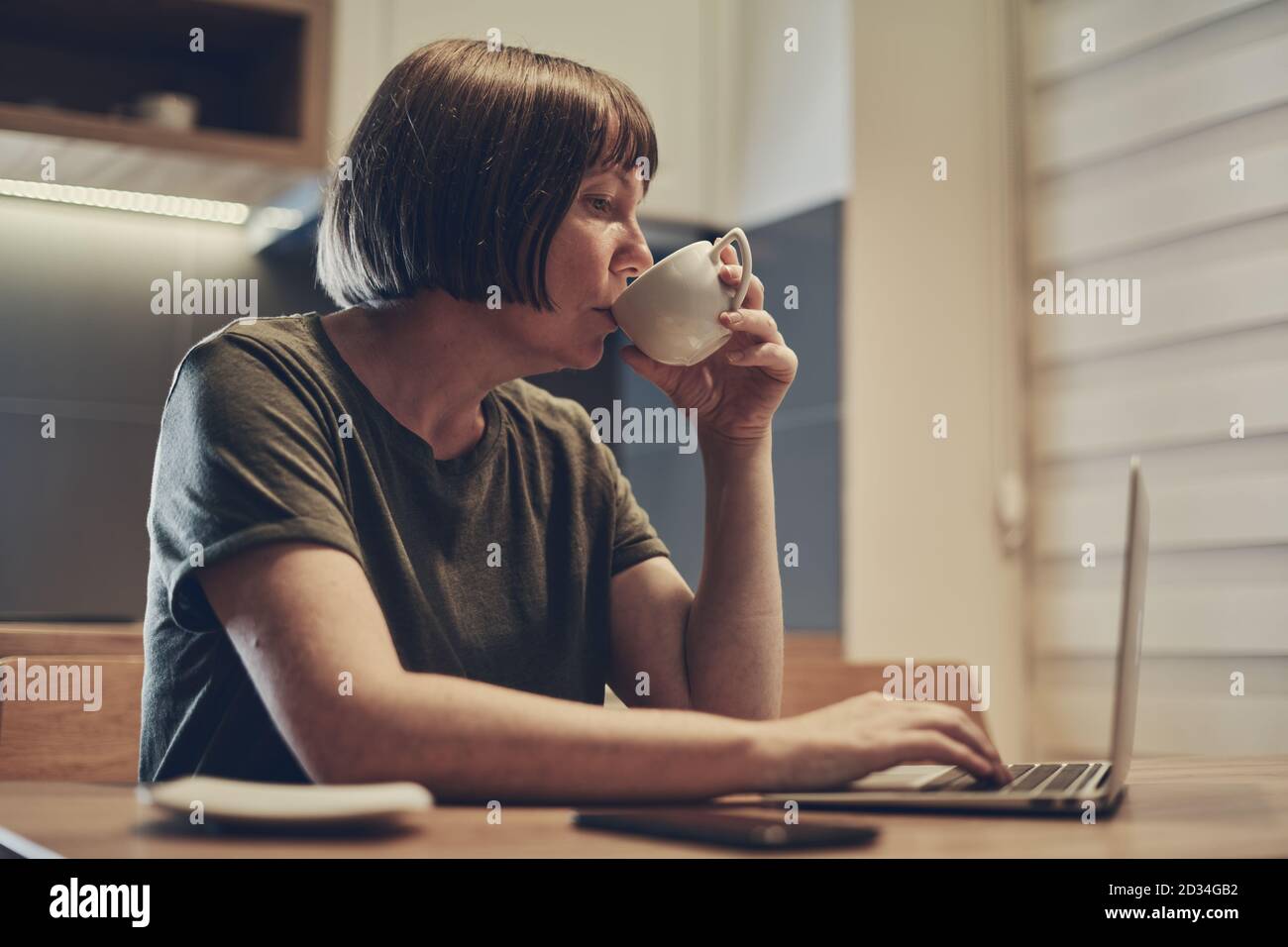 Freiberufliche Mitarbeiterin, die spät in der Nacht von zu Hause aus arbeitet und trinkt Kaffee, während Sie auf den Laptop-Bildschirm schauen Stockfoto