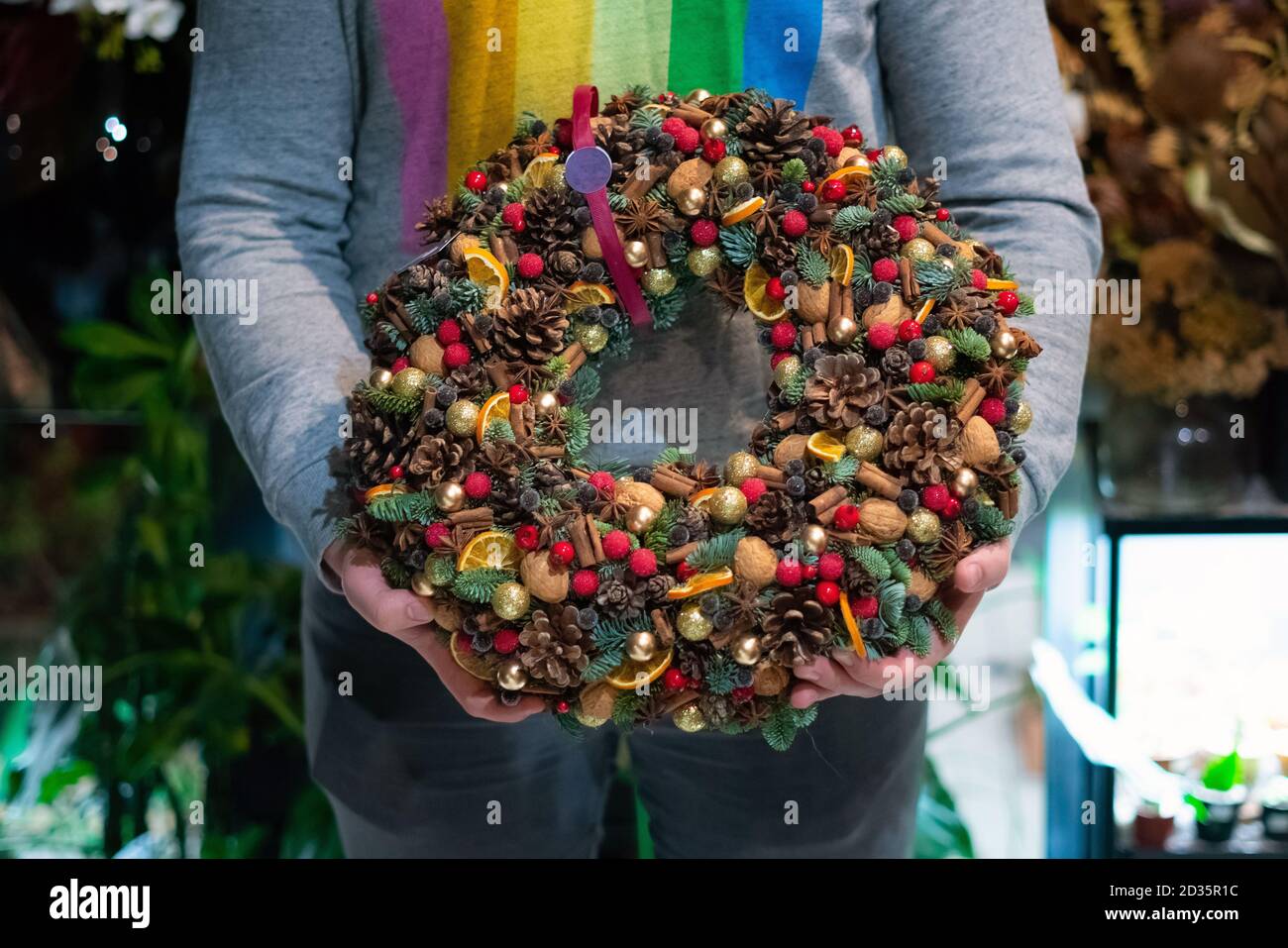 Person hält schöne und bunte Hand gemacht Weihnachtskranz, grüne Fichtenzweige mit Tannenzapfen und andere Dekorationen dekoriert. Weihnachtslch Stockfoto