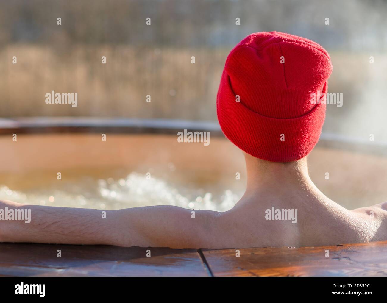 Junger Erwachsener, der draußen im Wannen-Whirlpool aus Holz entspannen und die Natur betrachten kann. Person, die an einem sonnigen Tag einen heißen Dampfpool genießen, private Spa-Behandlung Stockfoto