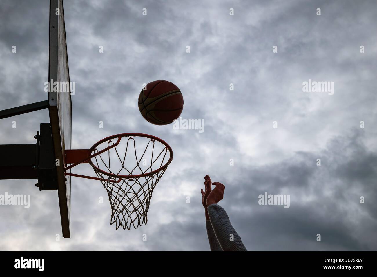 Dunkle Silhouette der Straße Basketball fällt in den Reifen an einem bewölkten Tag. Nahaufnahme eines Balls über dem Netz. Konzept des Erfolgs, Scoring po Stockfoto