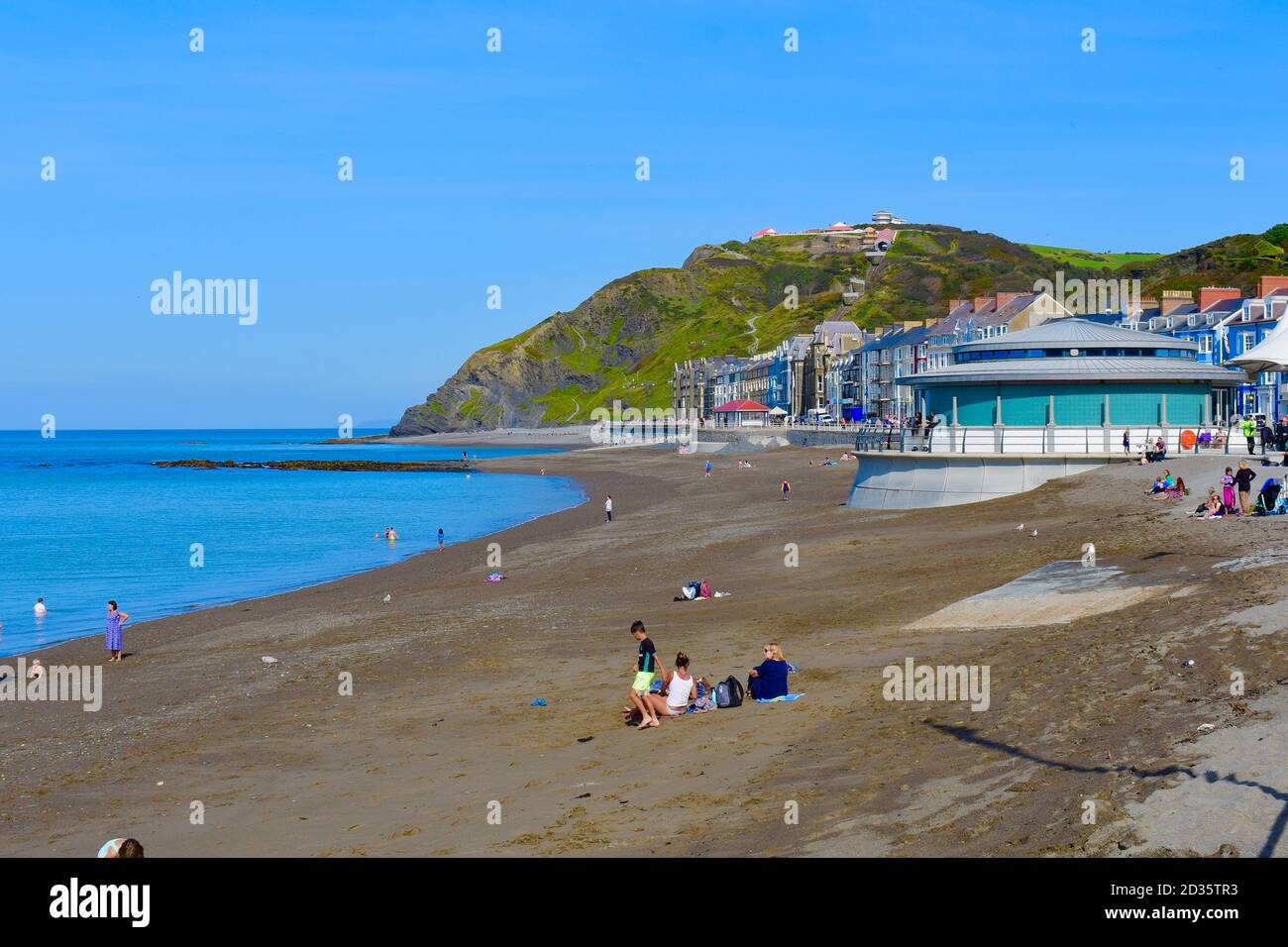 Die Strandpromenade & Strand in Aberystwyth.Menschen am Strand im Spätsommer Sonnenschein. Constitution Hill im Hintergrund mit Klippenbahn nach oben. Stockfoto