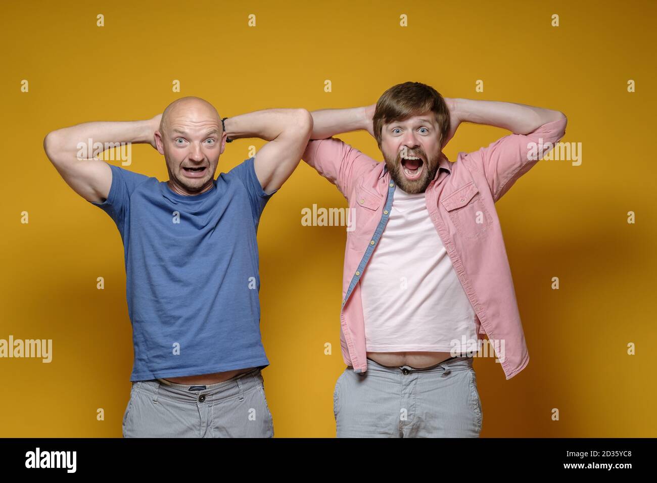 Zwei seltsame, fröhliche Männer halten ihre Hände hinter dem Kopf, schreien und schauen überrascht auf die Kamera. Stockfoto