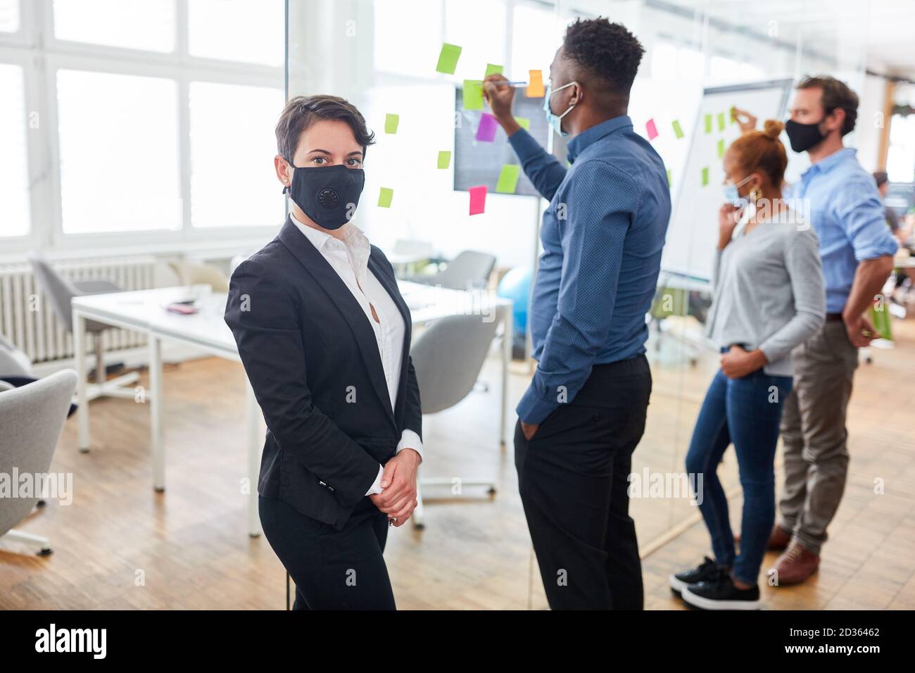 Geschäftsfrau mit Gesichtsmaske wegen Covid-19 Brainstorming mit Team Stockfoto