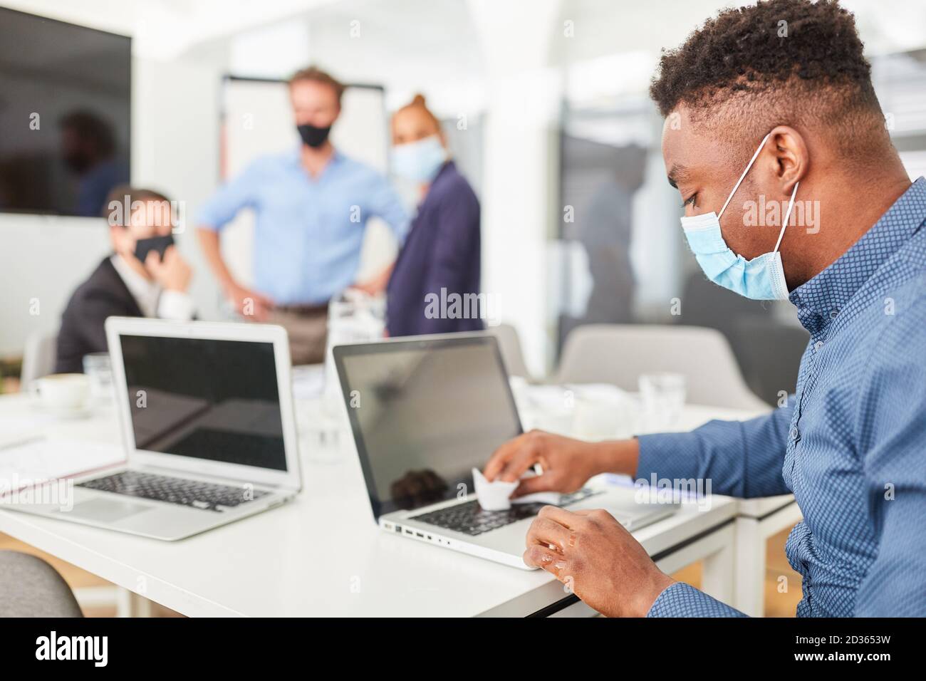 Business-Mann mit Gesichtsmaske bei der Arbeit während der Desinfektion Laptop Stockfoto