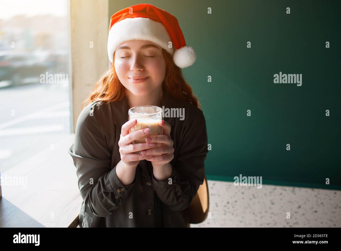 Weibliche Modell in weihnachtshut hält eine Tasse mit Kaffee in der Hand. Die junge Frau schloss die Augen und lächelte Stockfoto