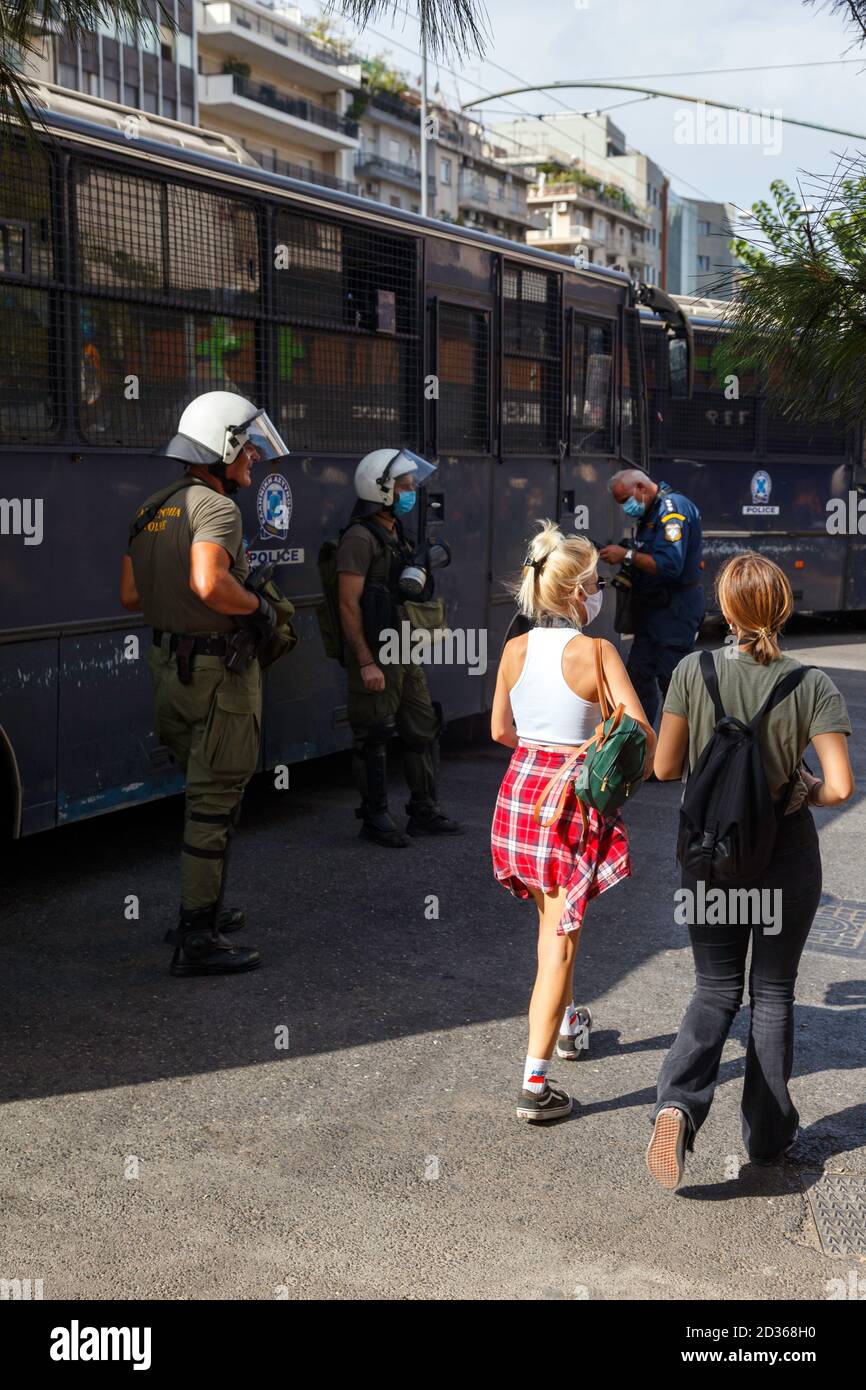 Polizeibeamte sind während eines Protestes in Alarmbereitschaft, während sie das Urteil des Prozesses der Goldenen Morgenröte in Athen, Griechenland, abwarten. Zwei junge Mädchen kommen vorbei. Stockfoto