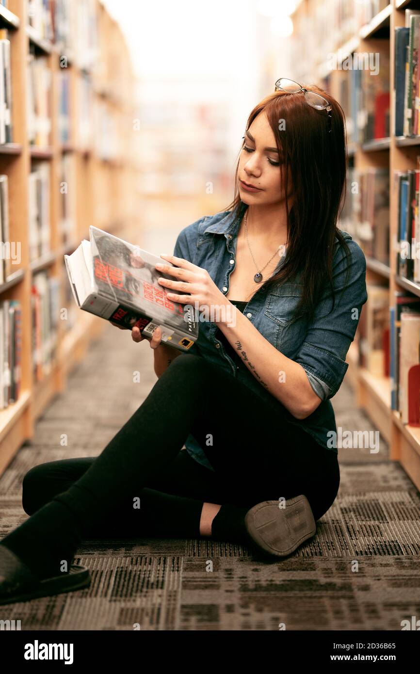 Eine einsame junge Frau durchsucht Bücher in ihrer lokalen Bibliothek mit Blick auf Bücherregale und Bücherregale. Stockfoto
