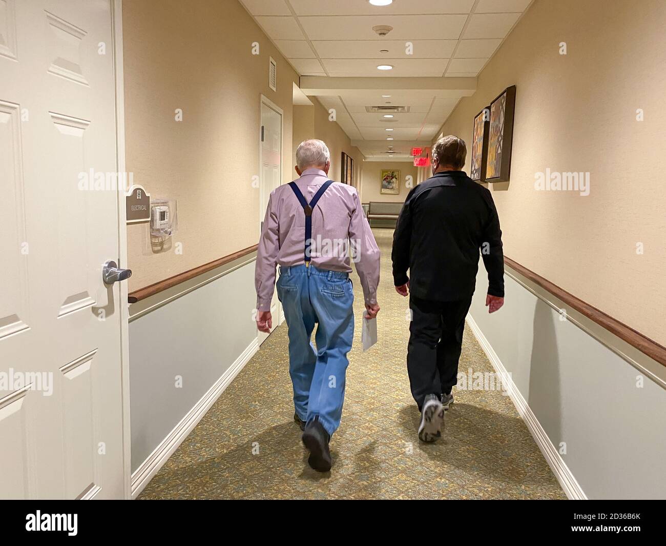Ein älterer Vater und Sohn, der in einem Flur einer Seniorenwohnanlage geht, Stockfoto