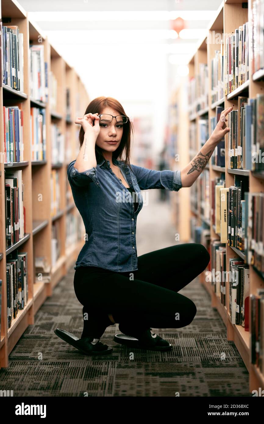 Eine einsame junge Frau, die in ihrer örtlichen Bibliothek Bücher durchstöbert, mit Blick auf Bücherregale und Bücherregale. Stockfoto