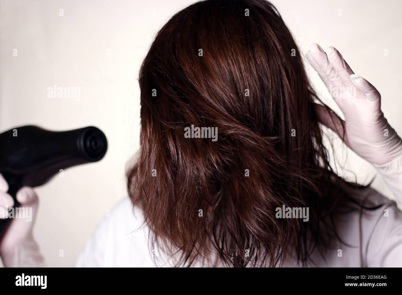 Erstellen Sie selbst-Frisur mit Haartrockner in Quarantäne. Hand in Latexhandschuhe mit Haartrockner. Selektiver Fokus. Teilsatz. Stockfoto