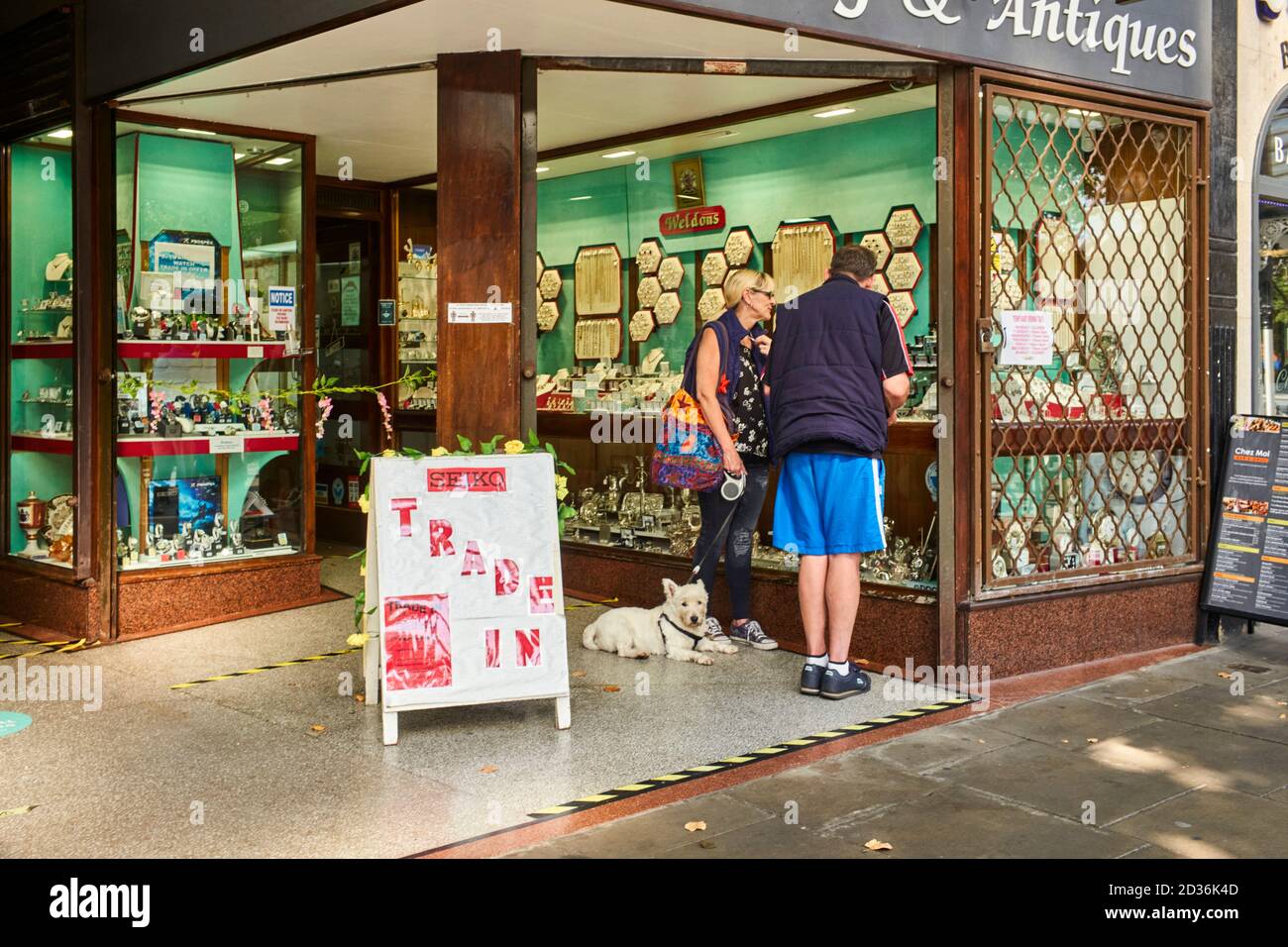 Ein älteres Paar mit einem Hund, der in einen Juwelier schaut Schaufenster in der Haupteinkaufsstraße in Southport Stockfoto
