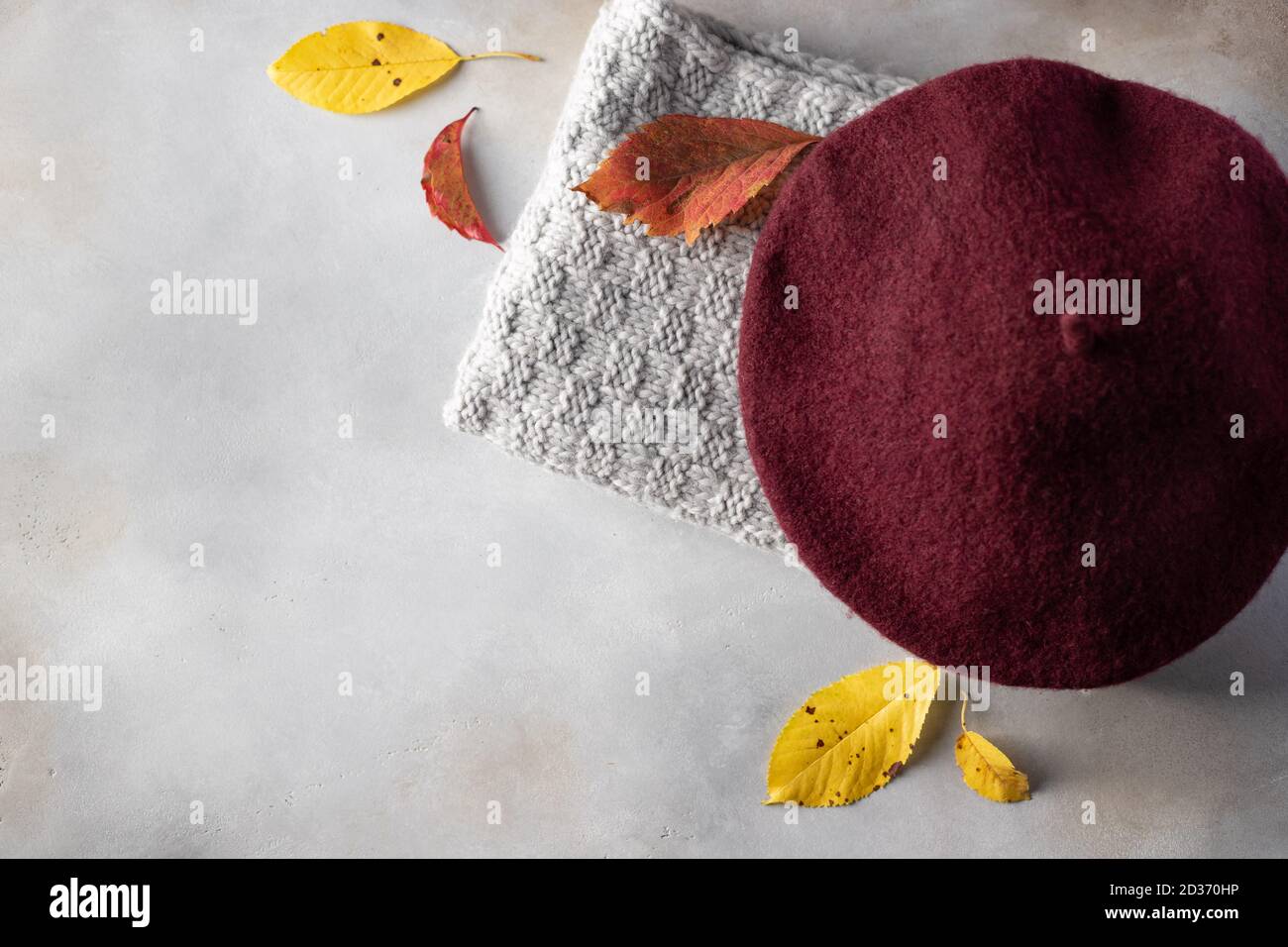 Hintergrund mit warmem Strickschal, Mütze und Herbstblättern. Stockfoto
