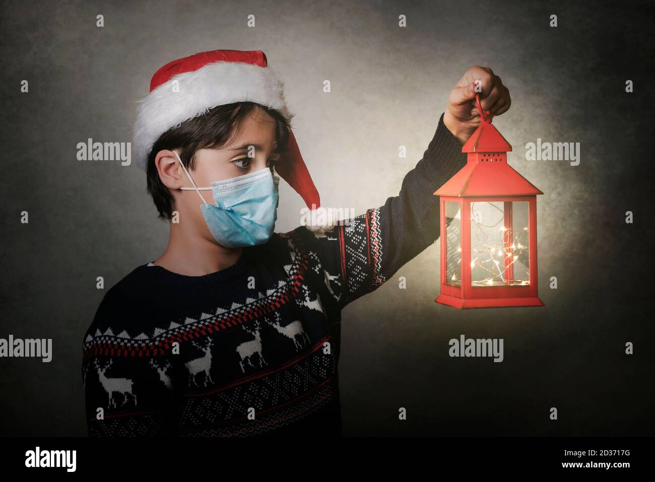 Frohe Weihnachten, Kind mit medizinischer Maske hält eine alte Laterne über Grauer Hintergrund Stockfoto