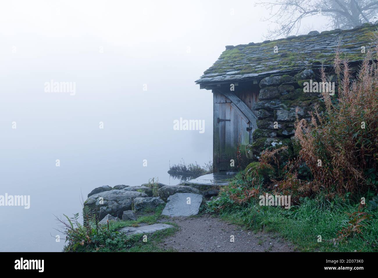 Grasmere, Cumbria, UK - 1/10/20: Ein Bootshaus, aus lokalem Stein gebaut, steht am Ufer von Grasmere in launischen frühen Morgenherbstlicht und Nebel. Stockfoto