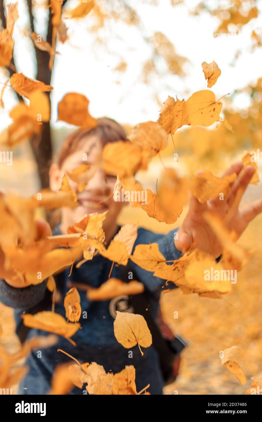 Glückliches Kind, das im Herbst im Wald mit Blättern spielt. Mädchen werfen trockene Blätter in die Kamera.Saisonale Outdoor-Aktivitäten mit Kindern. Erfassen Stockfoto