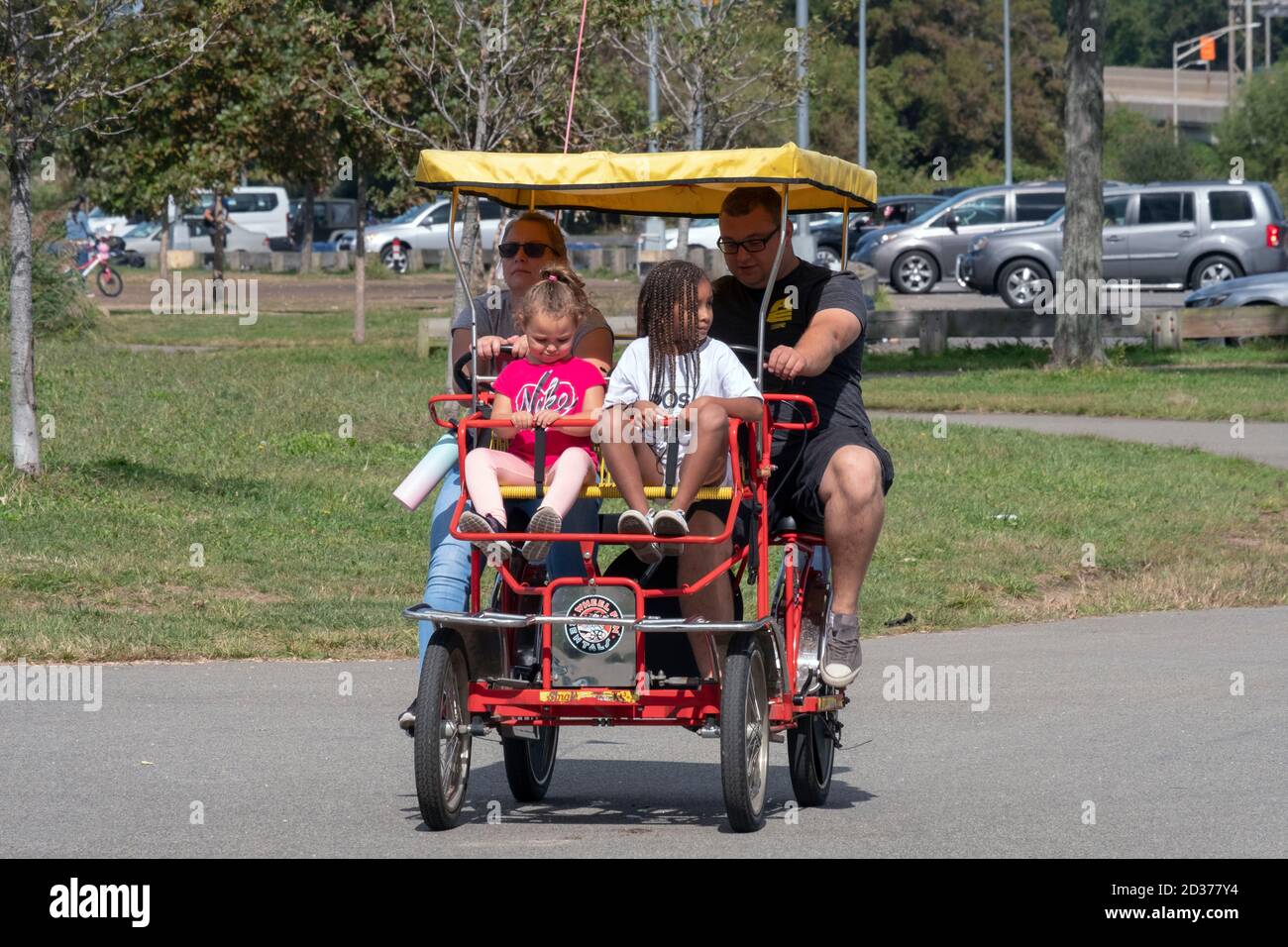 Eine vierköpfige Familie fährt im Flushing Meadows Corona Park in Queens, New York City, mit einem gemieteten Wheel Fun 4-Rad surrey. Stockfoto